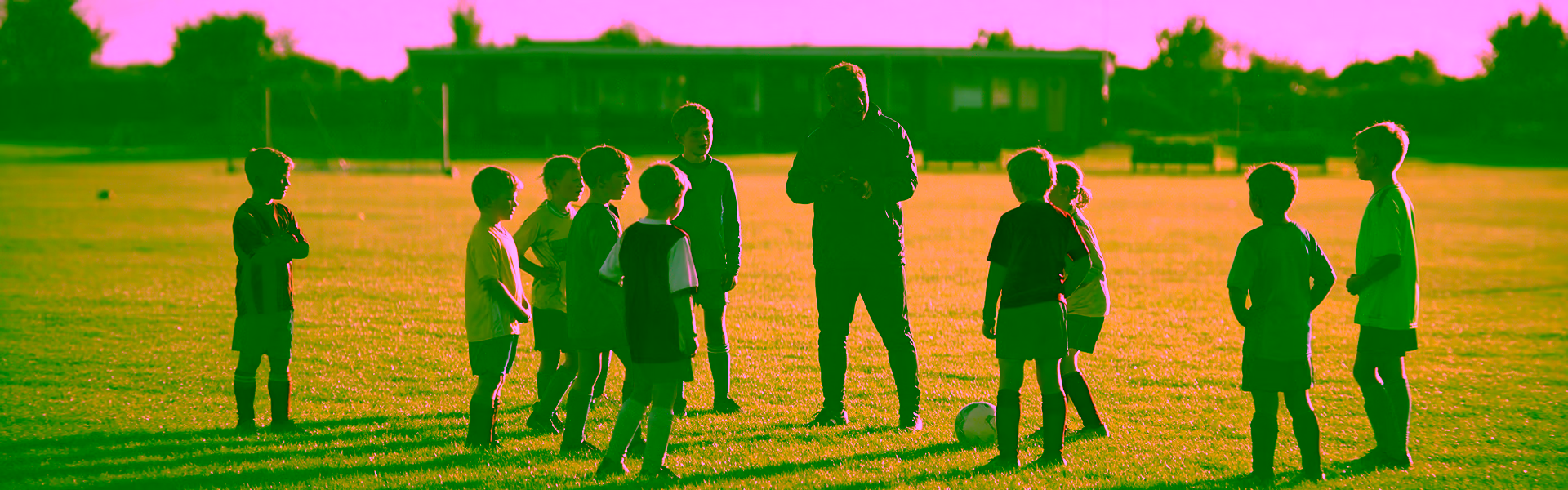 Ehrenamtlicher Jugendtrainer erklärt einer Gruppe Kinder auf dem Vereinssportplatz eine Übung
