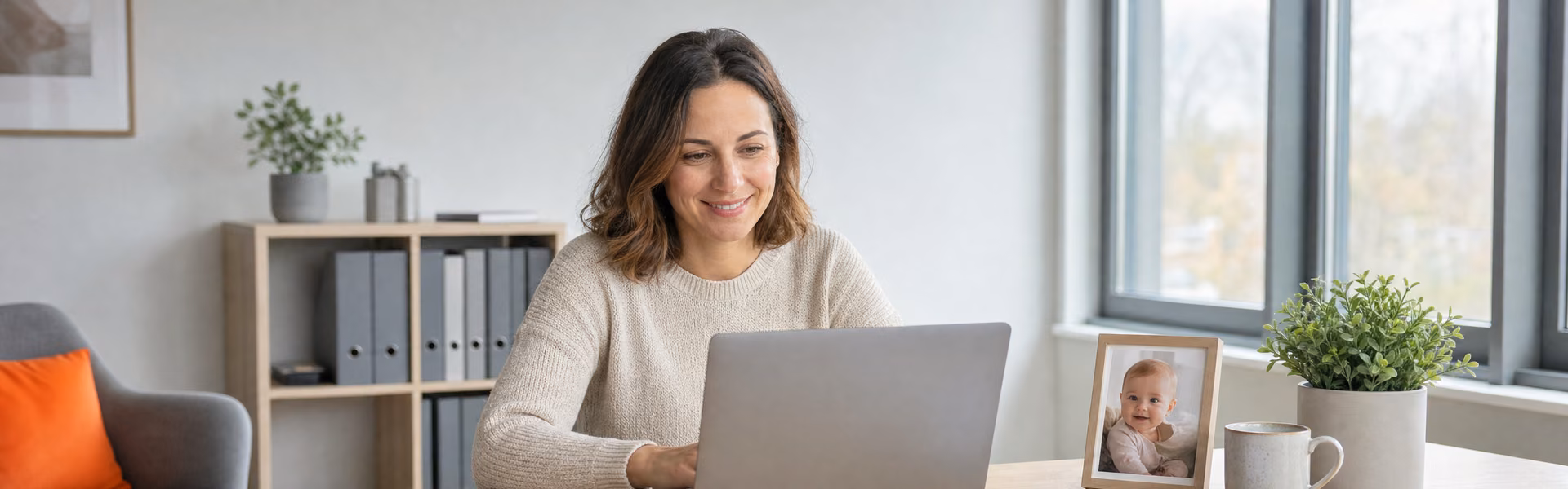 Mutter arbeitet nach der Geburt in Teilzeit im Büro am Laptop, auf dem Schreibtisch steht ein Foto ihres Babys